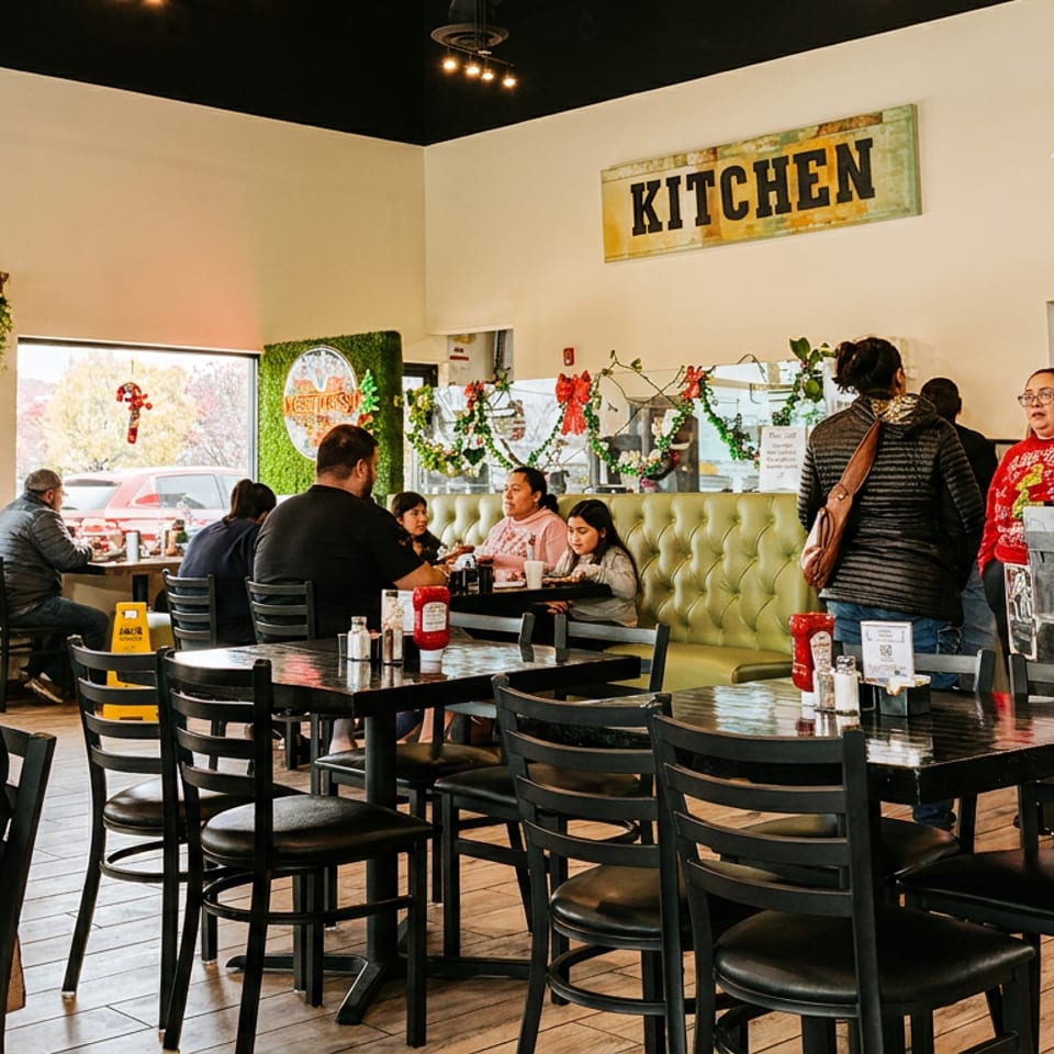 A bustling restaurant interior with customers dining at tables and a "Kitchen" sign overhead.