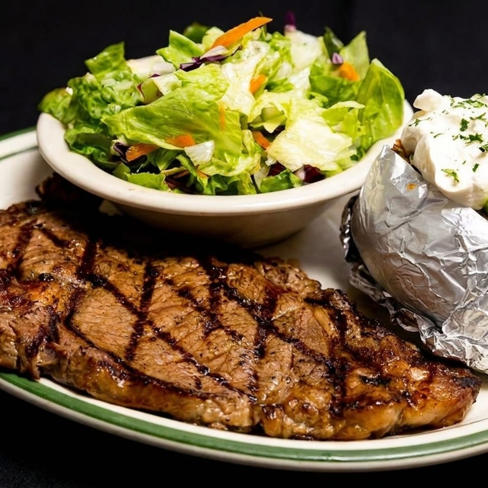 Grilled steak with grill marks, a side salad, and a foil-wrapped baked potato with toppings.